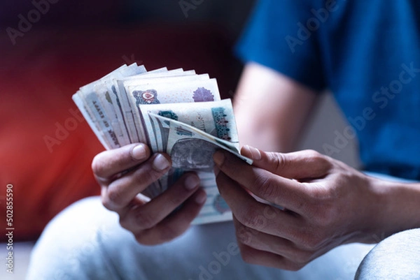 Obraz man holding and counting Egyptian paper currency 