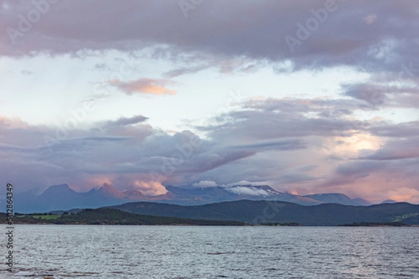 Fototapeta Evening landscape in Norway. Grey water of the fjord
Light blue sky with grey, pink and lilac clouds, misty mountains on the horizon