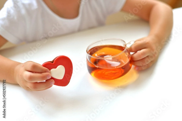 Fototapeta A girl in a white T-shirt holds a cup of tea and a liver in the form of a red heart. delicious sweet snack concept.