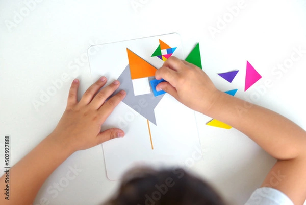 Fototapeta A preschooler girl sitting at the table collects a drawing from a geometric figure. the concept of early childhood development by montessori. a game of logic and imagination.