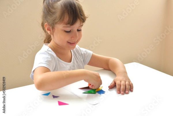 Fototapeta A preschooler girl sitting at the table collects a drawing from a geometric figure. the concept of early childhood development by montessori. a game of logic and imagination.