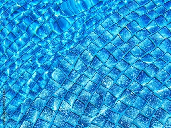 Fototapeta Overhead view of ripple surface water in blue swimming pool with many tiles at bootom.Swimming pool bottom caustics ripple and flow with waves background. Summer background. Texture of water surface.