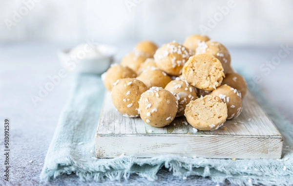 Obraz Traditional Indian festival sweets with coconut flakes on wooden board, light background. Laddoo or Laddu, Popular sweet snack in India. Vegan sweets.