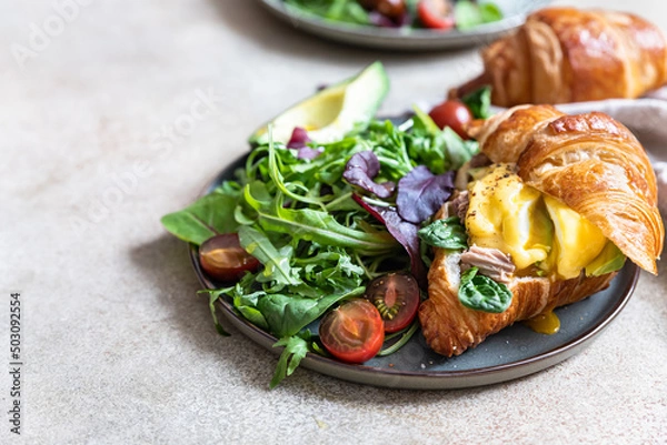 Obraz Croissant with tuna, poached egg, avocado and hollandaise sauce with salad leaves and tomatoes. Croissant sandwich with egg benedict and tuna.