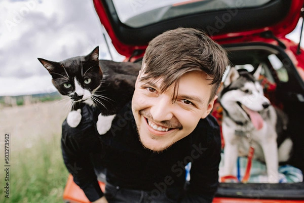 Fototapeta Husband cat on shoulders and husky dog in the background in the car.