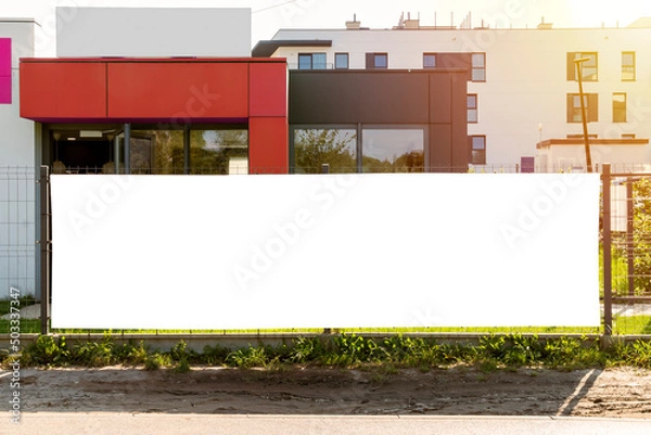 Obraz Blank white advertising banner on the fence in front of modern residential buildings