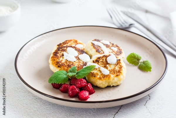 Fototapeta Cottage cheese pancakes with sour cream, raspberries and mint on a plate on the table.