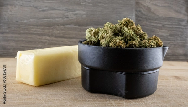 Fototapeta Assorted cannabis hemp flower in a measuring cup with a stick of butter. Wooden background