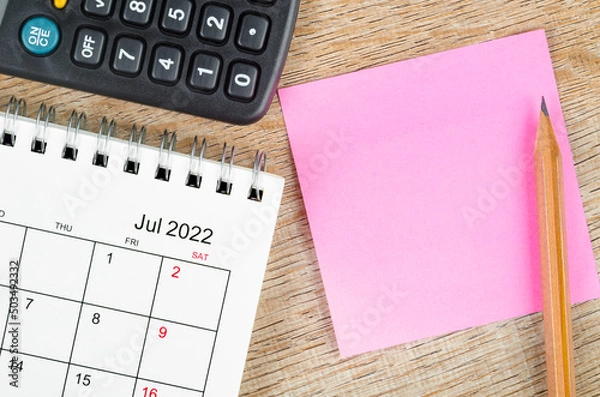 Fototapeta Blank sticky note on July 2022 desk calendar on wooden background for your text.