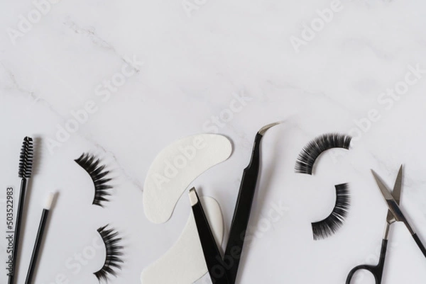 Fototapeta Beauty concept image including tools, products and equipment for eyelash extensions. Black and white colour theme set against a white background with copy space.
