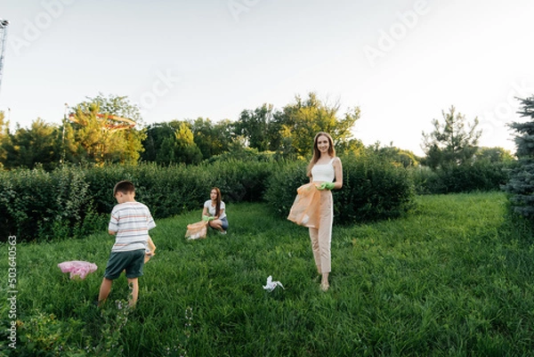 Fototapeta A group of adults and children together at sunset is engaged in garbage collection in the park. Environmental care, waste recycling. Sorting garbage.