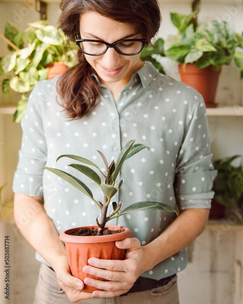 Obraz Smiling Beautiful female gardener in glasses take pot with plant and look dawn