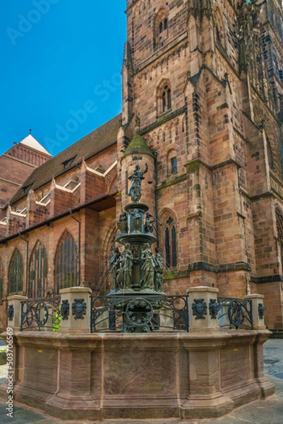 Fototapeta Nice view of the Virtue Fountain (Tugendbrunnen) in front of the church St. Lorenz in Nürnberg, Germany. The Late Renaissance fountain made of bronze presents personifications of the seven virtues.
