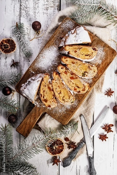 Obraz Christmas stollen on a cutting board. Wooden white table background. Traditional Christmas pastry with marzipan, nuts, raisins and dried fruit. Top view