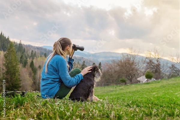 Fototapeta beautiful young girl with the dog looking through binoculars in nature in the mountains