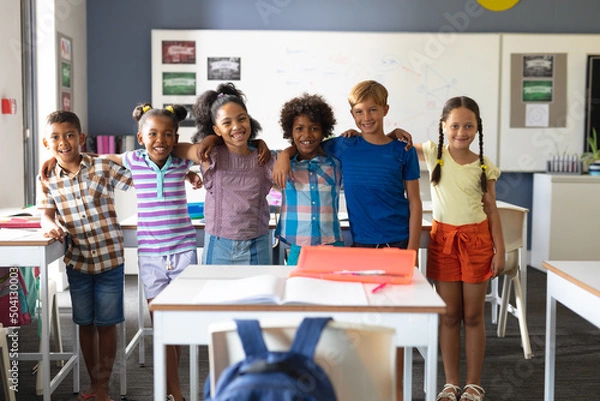 Obraz Portrait of smiling multiracial elementary school students standing with arm around in classroom