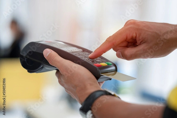 Fototapeta Cashier holding credit card reader machine on hand with insert card for payment process from customer, pressing the value number or price of products to charge the online payout, online deduction