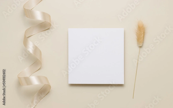 Fototapeta White invitation card mockup with lagurus grass top view, beige background