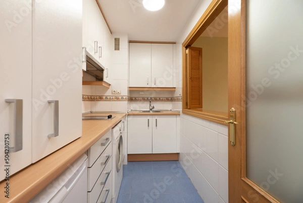 Fototapeta Full kitchen with white appliances, matching washer, wood-colored countertop, and Venetian-style serving hatch