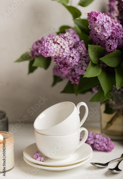 Obraz Tea set against the background of a spring bouquet of lilacs on a textured gray background. Composition with books and candles. Side view. Place to copy.