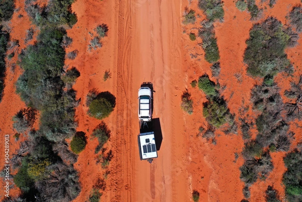 Fototapeta Aerial landscape drone view of 4WD vehicle towing an off road caravan driving on a sand dirt road