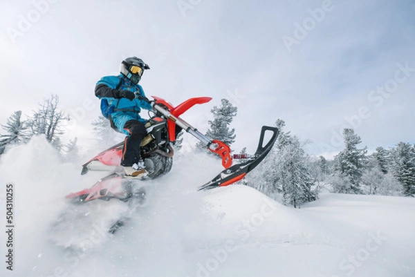 Fototapeta Motorcyclist jumping on snowbike in snow splashes in deep snow dust on winter day