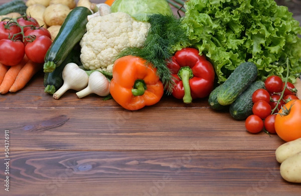 Fototapeta A set vegetables on a wooden background: carrots, potatoes, zucchini, paprika, cucumber, garlic, tomatoes, lettuce.Healthy food concept with vegetables and ingredients for cooking. Top view.Copy space