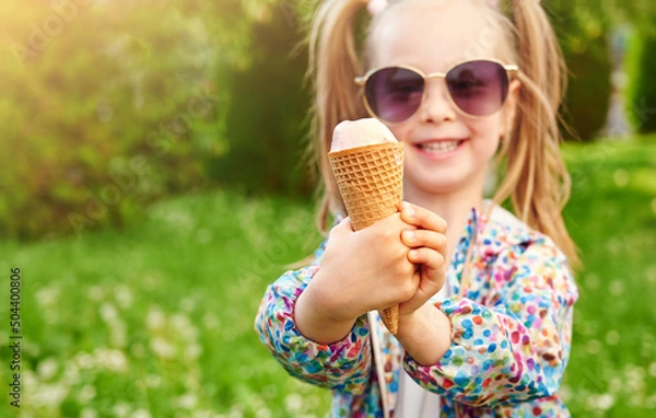 Fototapeta Close-up ice cream in a waffle cone in the hand with. Cheerful smiling child is holding it on summer green lawn background. Vacation and summer time concept