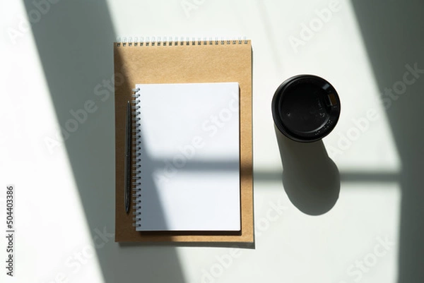Fototapeta a glass of coffee and a notepad with a pen. craft notepad with pen and cappuccino in sunlight on a white background with beautiful shadows.