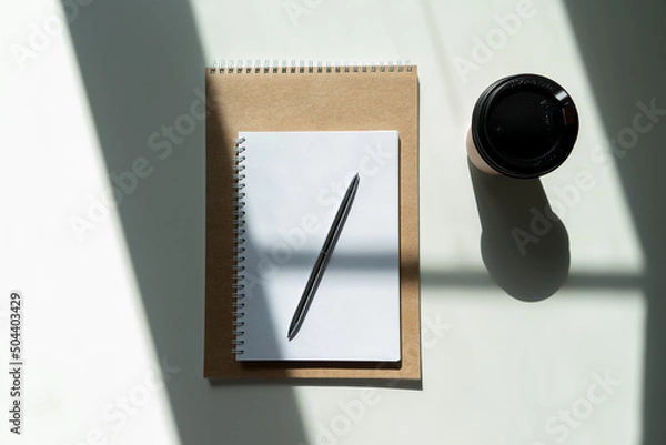 Fototapeta a glass of coffee and a notepad with a pen. craft notepad with pen and cappuccino in sunlight on a white background with beautiful shadows.