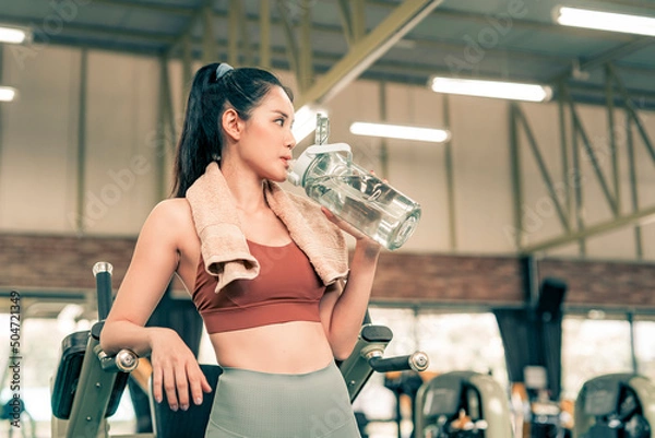 Obraz Fitness woman resting from excersise in the gym and drinking water from bottle.