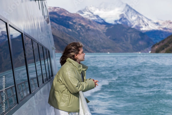 Fototapeta A girl on board a tourist boat admires the views of the lake and mountains on a sunny cold day, Argentina, El Calafate.
