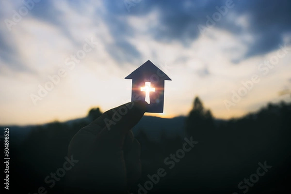 Obraz Hand holding home cross shapes. with light of sunset background,  christian silhouette concept.