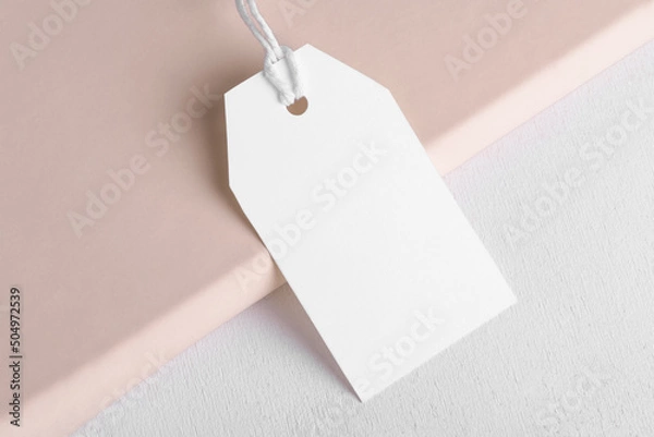Fototapeta Rectangle white gift tag mockup with white cord, close up on beige and white background. Blank paper rectangular price tag mockup, Sale and Black Friday concept, element for design, label mockup