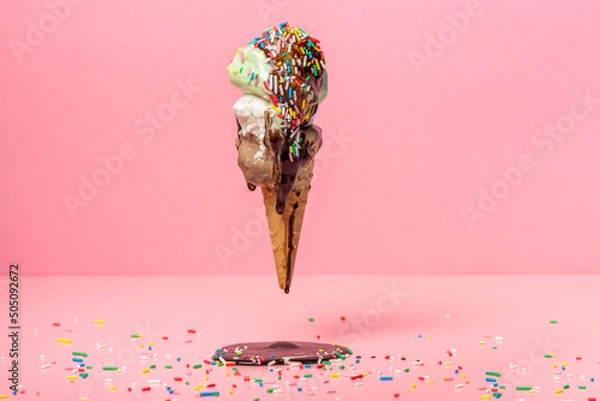 Obraz funny creative concept of flying wafer cone with ice cream covered, strewed sprinkles and poured with chocolate icing on pink background