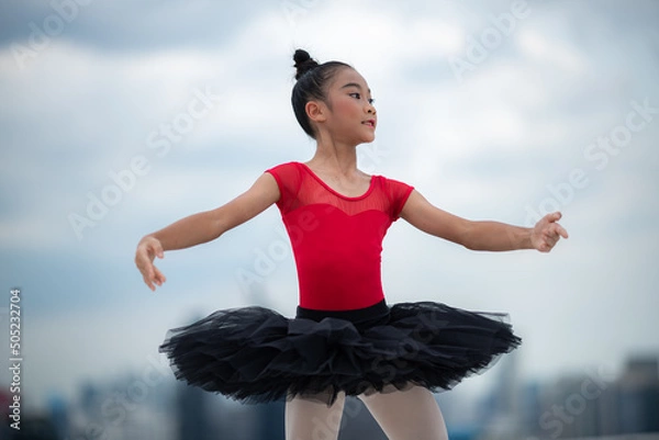 Fototapeta Cute little ballet dancer performing handstand posture while practicing dance form on terrace wearing ballerina costume