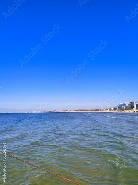 Fototapeta The Black Sea in spring with waves and sand on the beach with a bright blue sky.