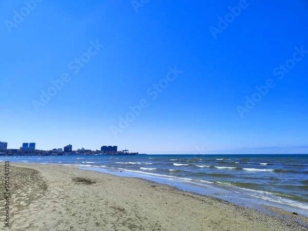 Fototapeta The Black Sea in spring with waves and sand on the beach with a bright blue sky.