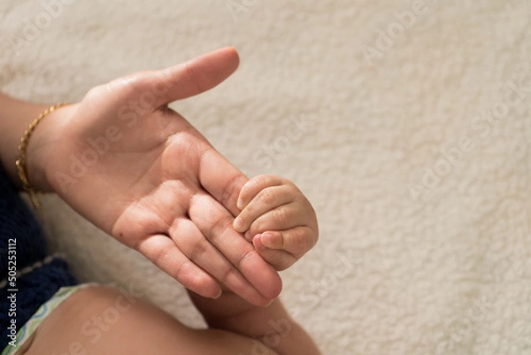 Fototapeta Closeup of Latin Mother holding hand of baby happy at bed