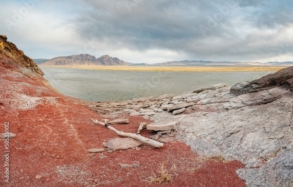 Obraz The shore of the Krasnoyarsk reservoir without water, red stones, clay and driftwood on the shore, rainy sky over Mount Tepsey Tepsey