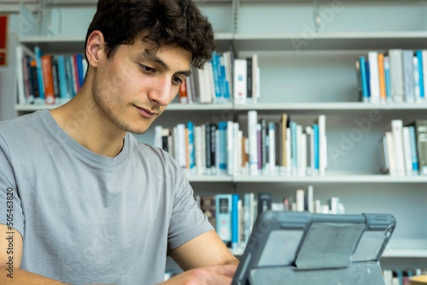 Obraz Young male student using a tablet in a library