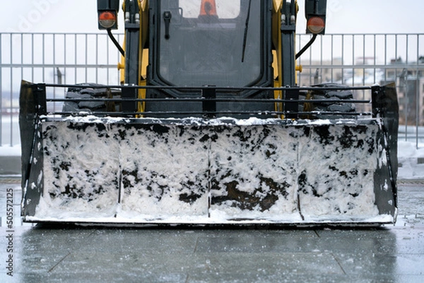 Obraz Snow plow tractor with a bucket in the snow remnants in the parking lot. Front view. Close up.