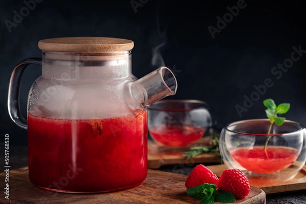 Fototapeta Flavored raspberry tea in a teapot with mint and whole berries. Vitamin hot steaming drink with natural berries