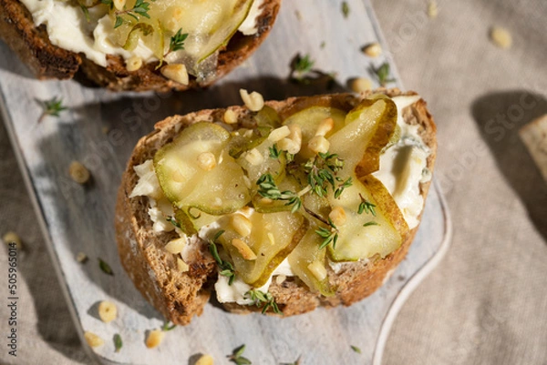 Fototapeta Bruschetta with gorgonzola cheese and pears, nuts on wooden table with textile, glass of white wine and beautiful flowers. Selective focus, copy space. 