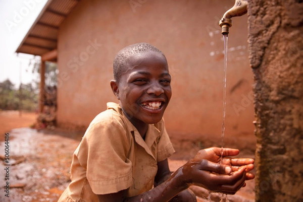 Obraz Smiling black african schoolboy drinking from a tap outside during recreation