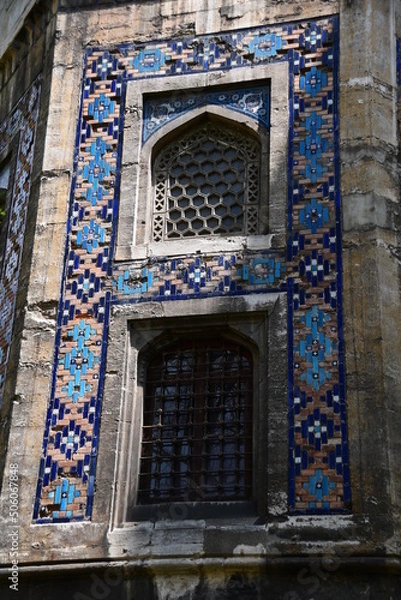 Fototapeta Windows with beautiful openwork lattices. Wall of an old building with colored tiles