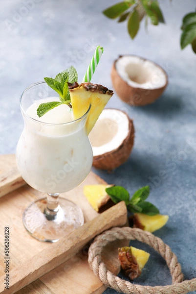 Fototapeta Summer. Drinks and cocktails. Pina colada in glass with pineapple, coconut, mint and a branch of greenery on a light gray background. Background image, copy space