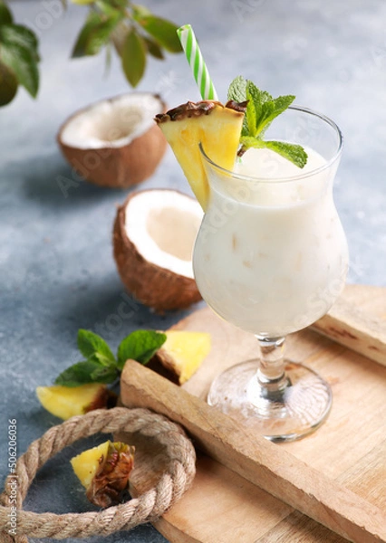 Fototapeta Summer. Drinks and cocktails. Pina colada in glass with pineapple, coconut, mint and a branch of greenery on a light gray background. Background image, copy space