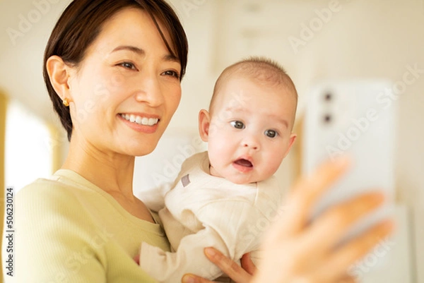 Obraz 赤ちゃんを抱っこしながら携帯電話を操作する母親