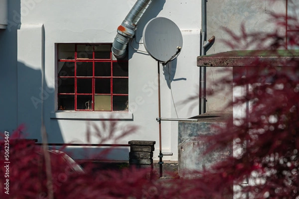 Fototapeta Satellite dish in the yard of a workshop and ventilation pipe through the mesh window - blurry reddish foreground